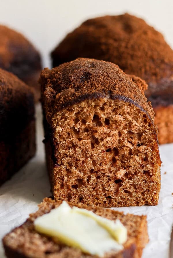 Close-up of sliced brown bread, with a pat of butter melting on one slice. Another knife lies nearby on a white surface.