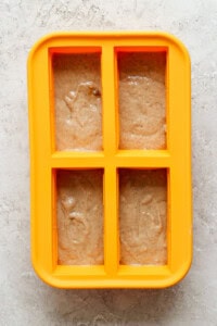 A yellow four-section silicone mold is filled with light brown batter on a light gray textured surface.