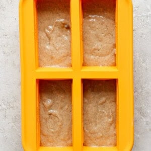 A yellow four-section silicone mold is filled with light brown batter on a light gray textured surface.