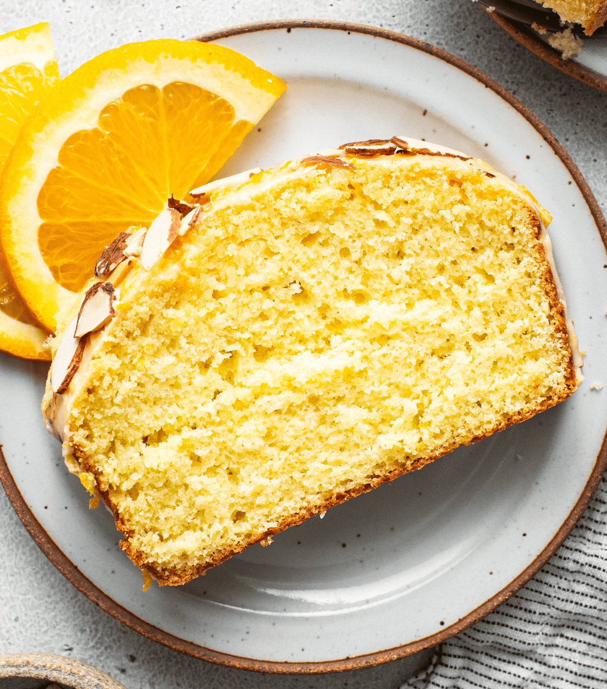 A slice of almond-topped cake on a plate with orange slices as garnish, a picture-perfect treat any fit foodie finds irresistible.