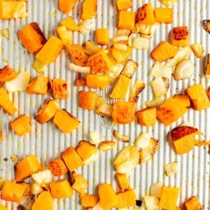 Diced butternut squash and chopped onions spread out and roasted on a baking sheet.