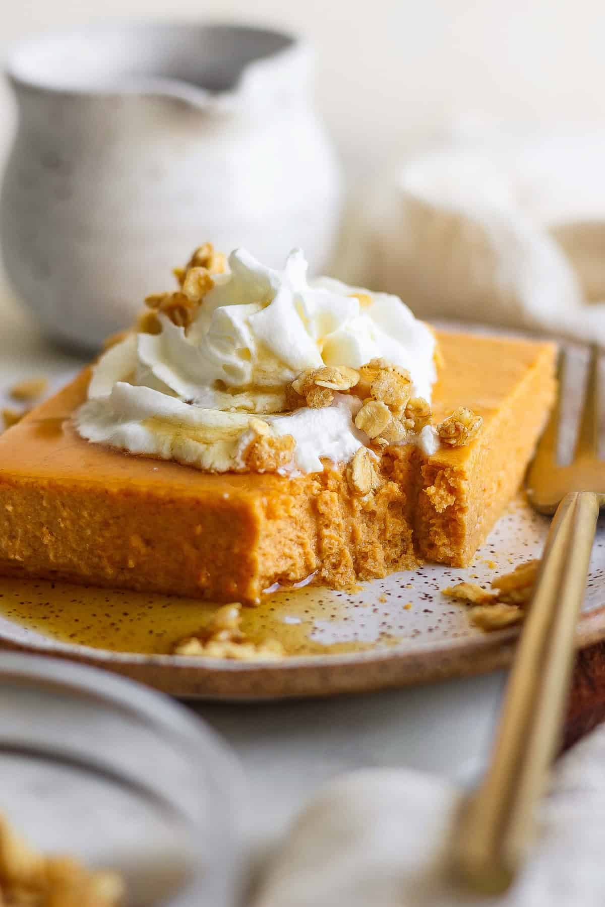 A slice of pumpkin cheesecake topped with whipped cream, granola, and drizzled with syrup, on a plate with a fork.