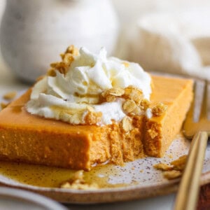 A slice of pumpkin dessert topped with whipped cream and granola on a plate, with a fork beside it. A small portion is missing from the dessert.