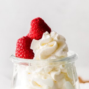 A glass container filled with whipped cream, topped with two fresh raspberries.