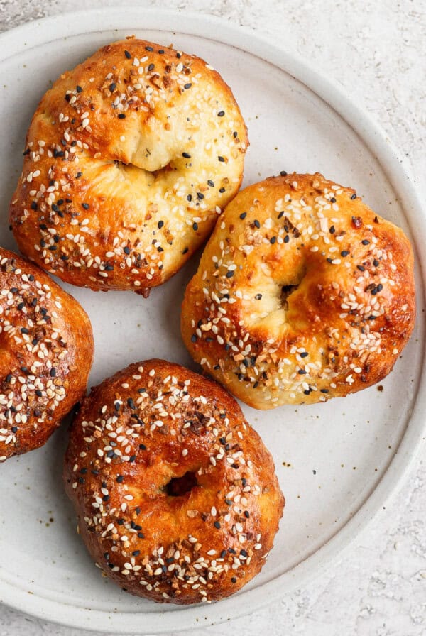 A white plate with four baked bagels topped with sesame seeds and seasonings.