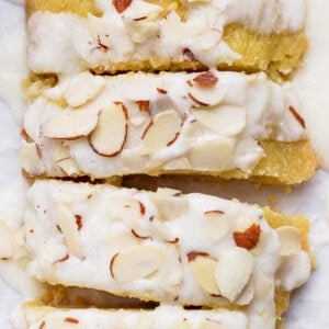 Sliced almond cake topped with white icing and sprinkled with almond slivers.