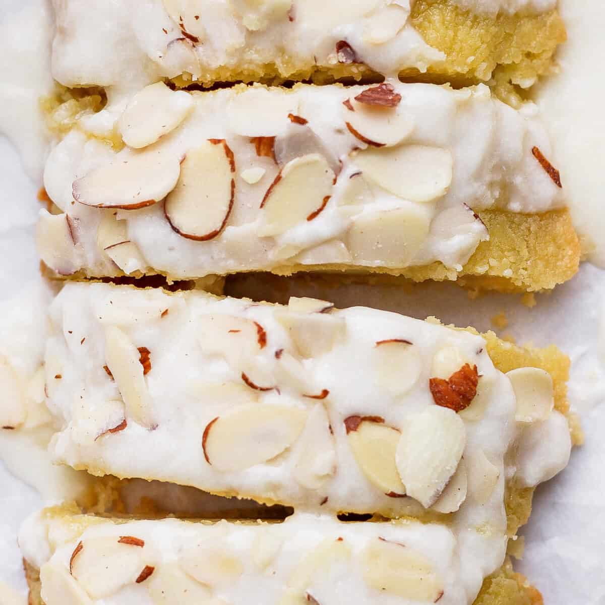 Close-up of almond-topped biscotti with a white icing drizzle. The biscotti pieces are stacked closely together, showcasing the almond slices and the glossy icing.