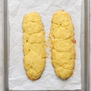 Two homemade almond biscotti cookie logs on a parchment-lined baking sheet.