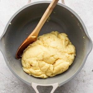 A wooden spoon rests in a pot containing a cooked dough mixture.