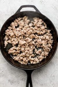 Ground meat cooking in a black cast iron skillet on a light textured surface.