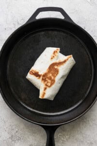 A folded and grilled burrito in a black cast iron pan on a gray surface.