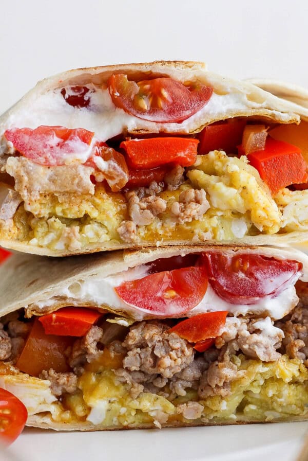 Two halves of a burrito with visible layers of tomatoes, ground meat, cheese, and sauce, placed on a white plate.