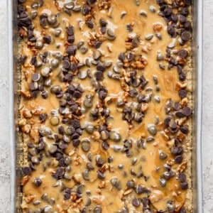 A baking tray filled with a dessert topped with melted caramel, chocolate chips, and chopped nuts.