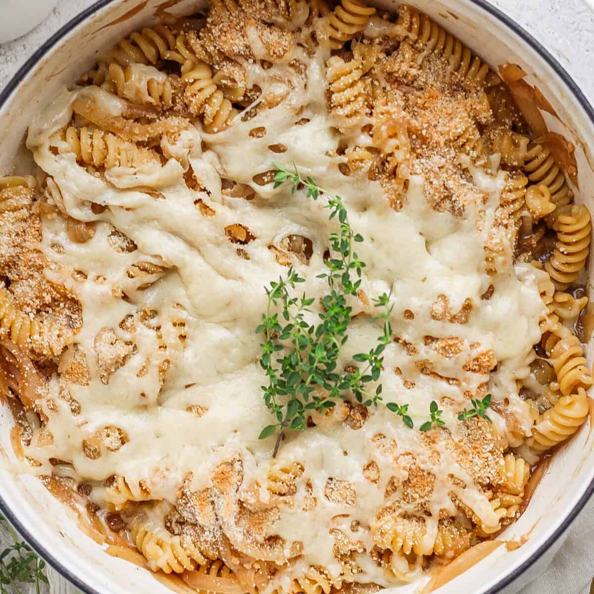 A close-up of a baked pasta dish with spiral noodles topped with melted cheese, breadcrumbs, and a garnish of fresh herbs.