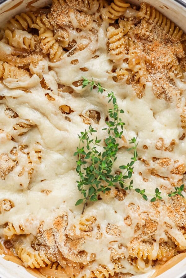 A close-up of a baked pasta dish with spiral noodles topped with melted cheese, breadcrumbs, and a garnish of fresh herbs.