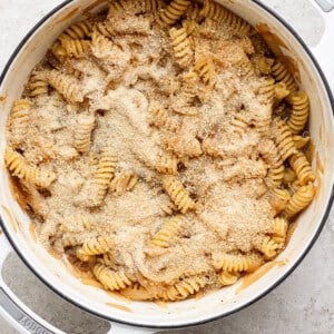 A pot of rotini pasta topped with a layer of grated cheese and breadcrumbs.