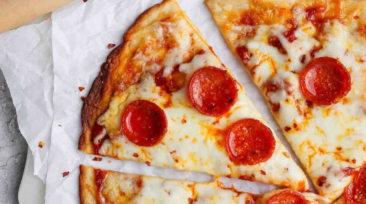Pepperoni pizza with melting cheese on parchment paper, slices slightly separated.