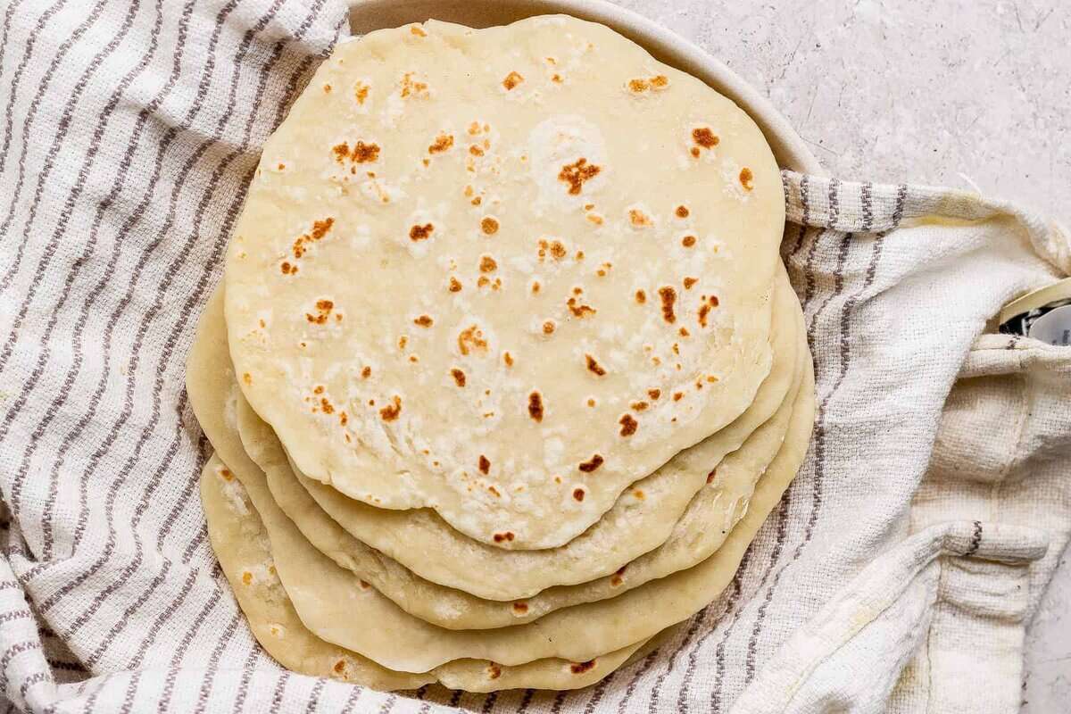 A stack of homemade flour tortillas rests on a striped kitchen towel.