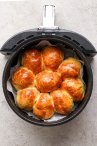 Golden brown homemade rolls arranged in a circular pattern inside an air fryer basket on a gray surface.