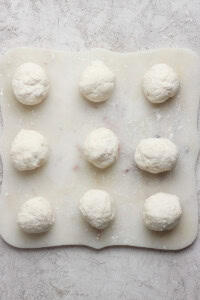 Nine dough balls on a floured surface, arranged in a 3x3 grid.