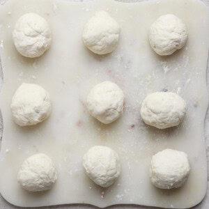 Nine dough balls on a floured surface, arranged in a 3x3 grid.