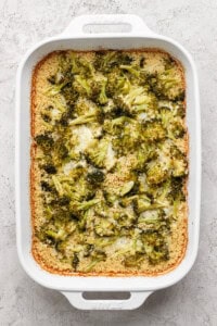 A white baking dish with broccoli casserole, featuring browned edges and a creamy texture.