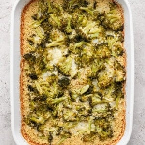 A white baking dish with broccoli casserole, featuring browned edges and a creamy texture.