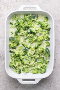 A white baking dish filled with fresh broccoli florets on a light textured background.