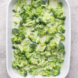 A white baking dish filled with fresh broccoli florets on a light textured background.