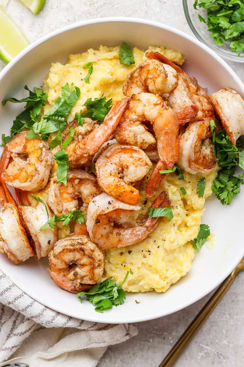 A white bowl filled with grilled shrimp on a bed of creamy grits, garnished with chopped parsley.