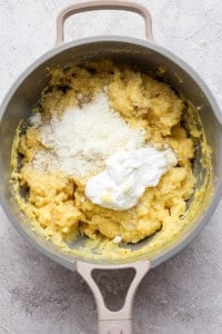 A pot containing a mixture of yellow mashed potatoes topped with grated cheese and a dollop of sour cream.