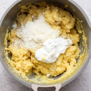 A pot containing a mixture of yellow mashed potatoes topped with grated cheese and a dollop of sour cream.