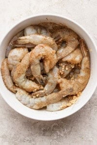 A bowl of raw shrimp seasoned with spices, ready for cooking.