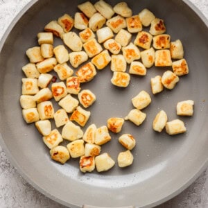 Pan with evenly browned gnocchi pieces on a light surface.