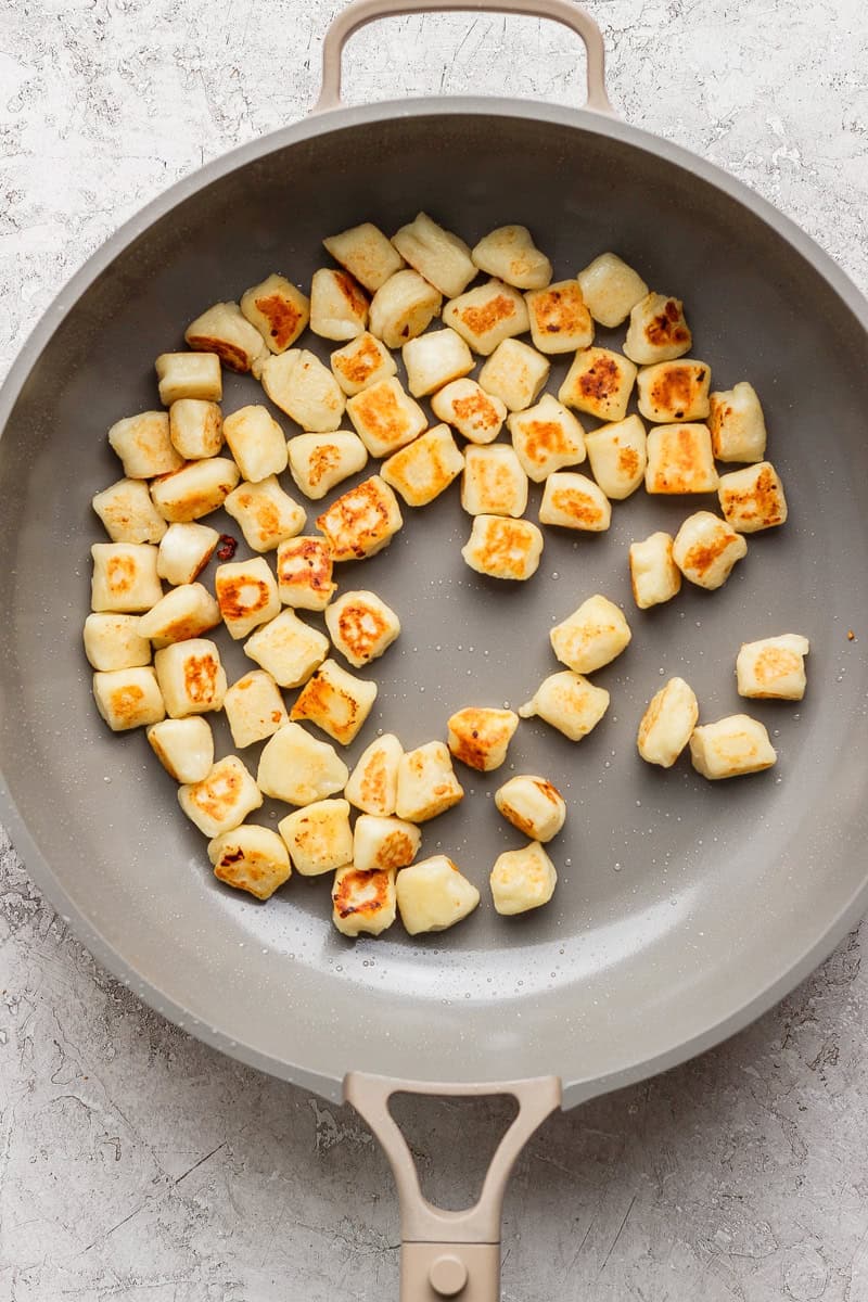 Pan with evenly browned gnocchi pieces on a light surface.