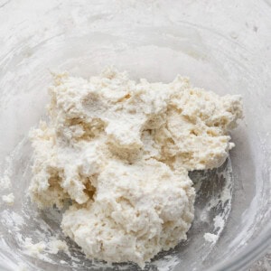 A clear bowl containing a mixture of flour and butter, forming a crumbly dough.