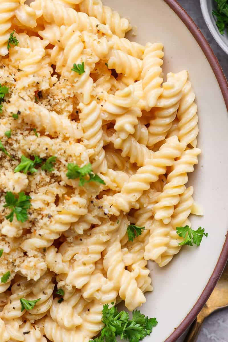 A close-up of a bowl of creamy pasta topped with breadcrumbs and garnished with fresh parsley.