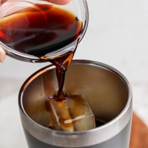 Pouring dark liquid into a stainless steel tumbler with ice.