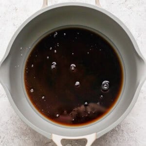 A gray pan containing dark liquid with a few bubbles on the surface, placed on a light gray textured background.