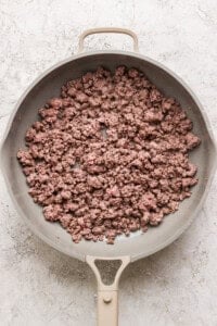 A frying pan containing cooked ground beef on a textured gray background.