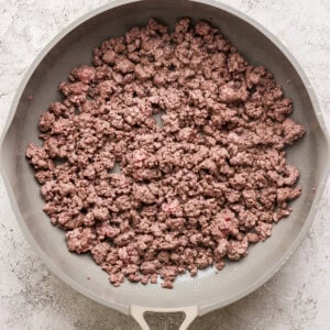 A frying pan containing cooked ground beef on a textured gray background.