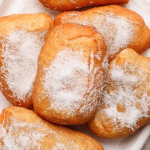 A pile of sugared beignets on a white surface.