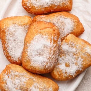 A plate of six sugar-dusted beignets on a white dish.