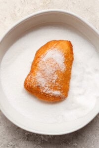 A sugar-covered pastry sits on a plate filled with granulated sugar.
