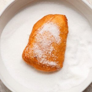 A sugar-covered pastry sits on a plate filled with granulated sugar.