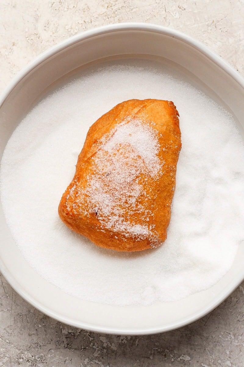 A sugar-covered pastry sits on a plate filled with granulated sugar.