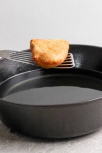 A golden-brown hash brown on a spatula over a black frying pan.
