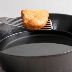 A golden-brown hash brown on a spatula over a black frying pan.