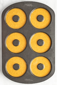 A six-cavity donut baking pan filled with pumpkin batter, ready for baking.