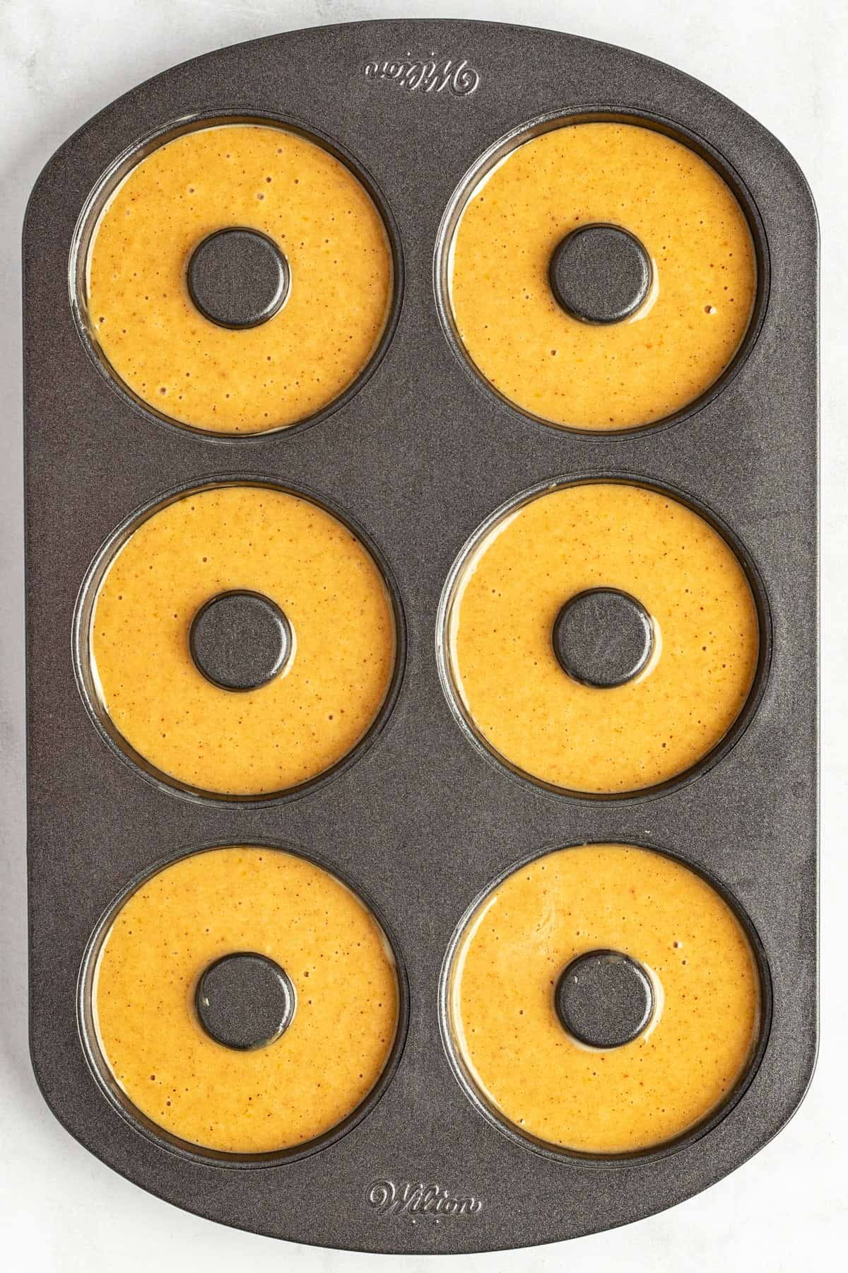 A six-cavity donut baking pan filled with pumpkin batter, ready for baking.